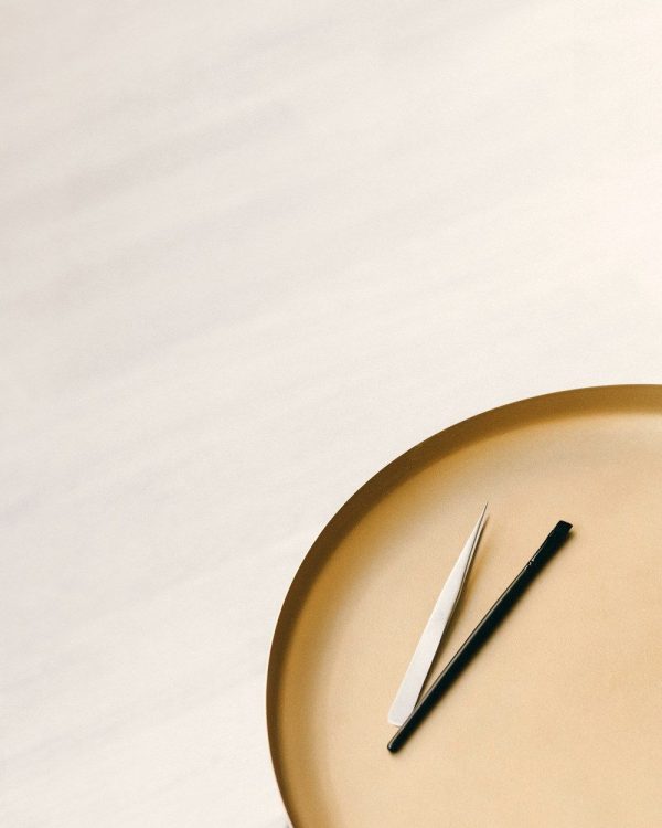 Stainless steel lash tweezers on a gold tray
